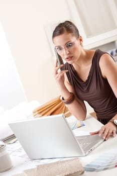 Young female designer on the phone at office with laptop