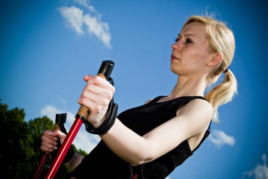 Nordic Walking - Young woman is hiking against blue sky.