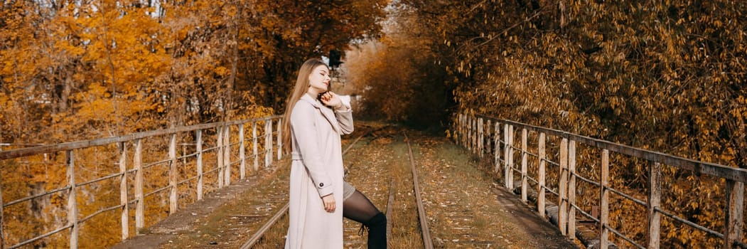 A beautiful long-haired woman walks through the autumn streets. Railway, autumn leaves, a woman in a light coat.