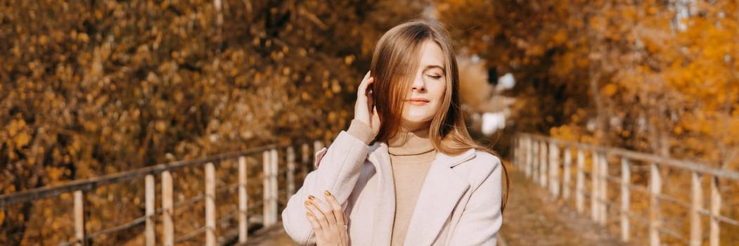 A beautiful long-haired woman walks through the autumn streets. Railway, autumn leaves, a woman in a light coat.