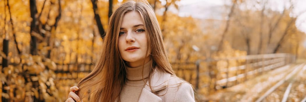 A beautiful long-haired woman walks through the autumn streets. Railway, autumn leaves, a woman in a light coat.