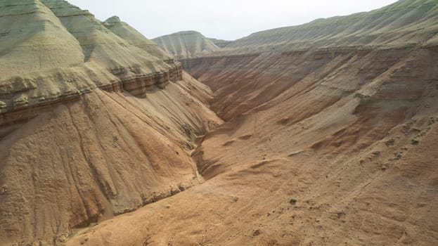 Colorful high mountains and a canyon made of clay. A large gorge with different rocks and different colors. Red, orange, white and yellow flowers of the walls of the rocks. A tourist walks. Aktau