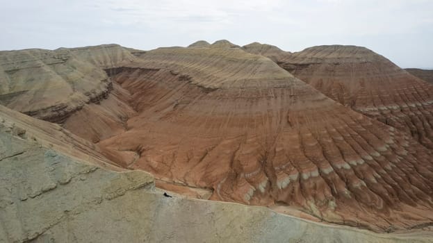 Colorful high mountains and a canyon made of clay. A large gorge with different rocks and different colors. Red, orange, white and yellow flowers of the walls of the rocks. A tourist walks. Aktau