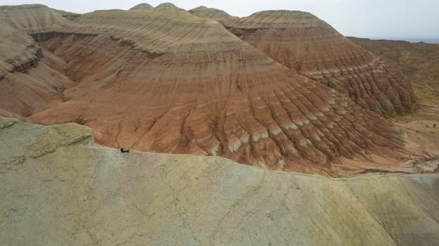 Colorful high mountains and a canyon made of clay. A large gorge with different rocks and different colors. Red, orange, white and yellow flowers of the walls of the rocks. A tourist walks. Aktau