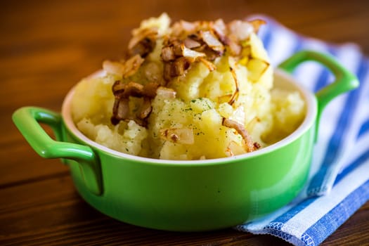 Cooked mashed potatoes with fried chopped bacon and onions in a bowl.