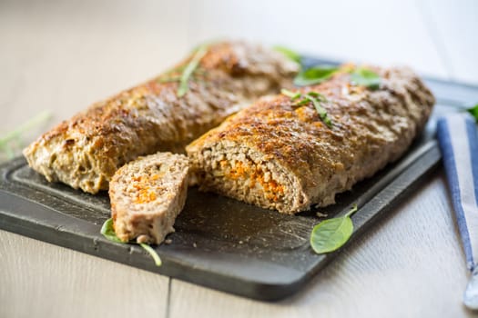 Cooked minced meatloaf with vegetable filling inside, on a wooden table.