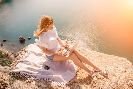 Freelance woman working on a laptop by the sea, typing away on the keyboard while enjoying the beautiful view, highlighting the idea of remote work