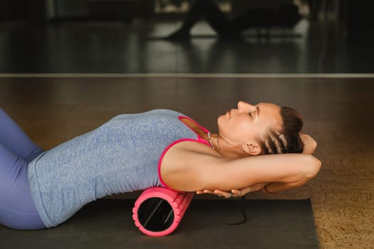 Slender girl doing yoga with a big massage roller on the floor.