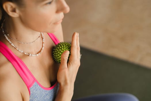 A woman does self - massage with a small ball while sitting in a fitness room . Myofascial relaxation.