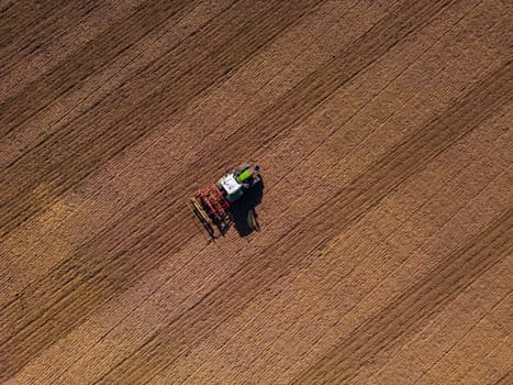 A tractor with plow on a field plowing from the ground directly from above with drone