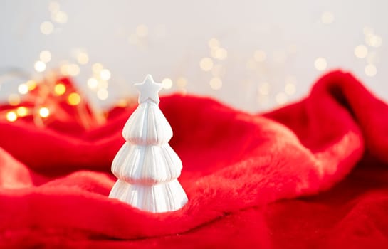 Christmas home interior with a white ceramic Christmas tree on a red plaid and bokeh with a garland in the background. Christmas and New Year concept