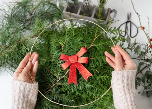 The concept of preparing for Christmas and New Year. A girl makes a Christmas wreath, the process of making a Christmas wreath from pine needles, thuja, shimia, rose hips, pine twigs