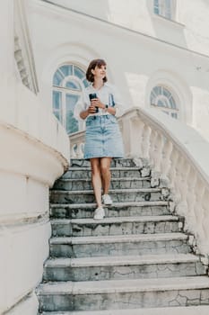 Woman staircase city. A business woman in a white shirt and denim skirt walks down the steps of an ancient building in the city.