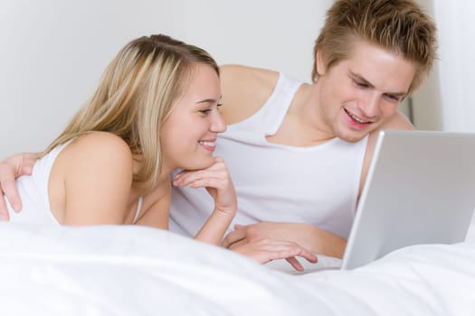Young couple relax in bed with laptop