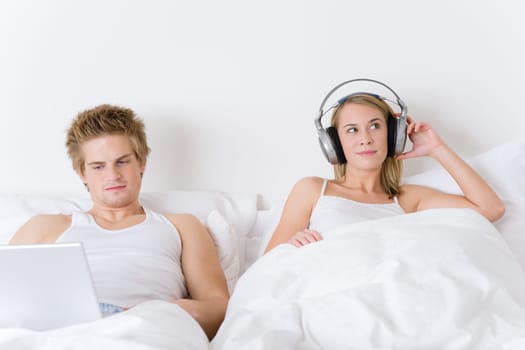 Young couple relax in bed with music and laptop