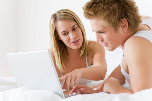 Young couple relax in bed with laptop lying down