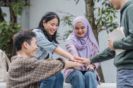 Image of a group of cheerful Asian college students putting their hands together, showing teamwork and unity..