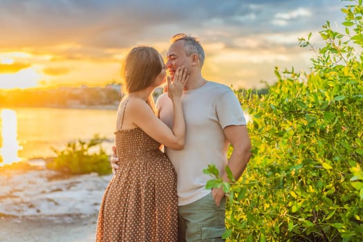 A happy, mature couple over 40, enjoying a leisurely walk on the waterfront On the Sunset, their joy evident as they embrace the journey of pregnancy later in life.