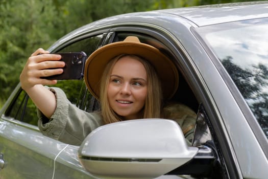 Blonde woman stoped car on road to take a selfie photo. Young tourist explore local travel making candid real moments. True emotions expressions of getting away and refresh relax on open clean air