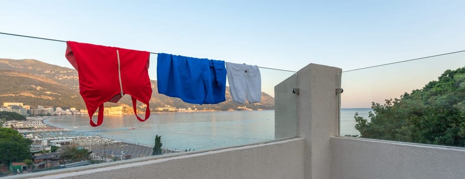Swimsuits dry on the glass railing of a modern balcony in the colors of the flags of Russia and