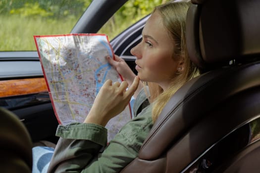 Blonde woman sitting inside the car checking the route on map to get to the destination. Afraid to get lost in forest. Young tourist explore local travel making candid real moments. True emotions expressions of getting away and refresh relax on open clean air