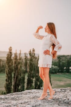 Romantic beautiful bride in white dress posing with sea and mountains in background. Stylish bride standing back on beautiful landscape of sea and mountains on sunset