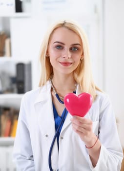 Female medicine doctor hands holding and covering red toy heart closeup. Cardio therapeutist student education physician make cardiac physical heart rate measure arrhythmia concept