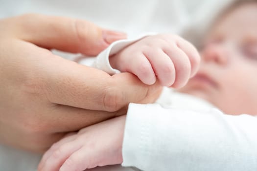 Close-up depicts a sleeping newborn's gentle hold on mother's finger, signifying pure love