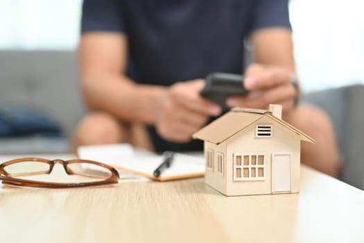 A house model, calculator and document on table with man sitting in background. Household finance concept.