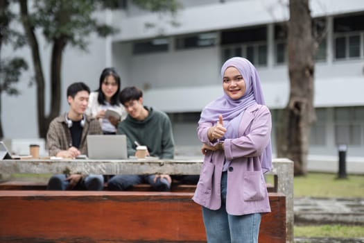 Portrait of a Muslim student with a fellow student behind him studying in the university garden. Young people spend time together, reading books, working on laptops, tablets..