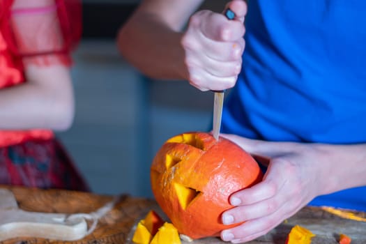 boy's hands carve out the pumpkin's eyes, Pumpkin head for Halloween decoration together with his sister at home in the kitchen, Close Up view, High quality photo