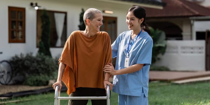 Nurse or caregiver help elderly walk by using walker in garden.