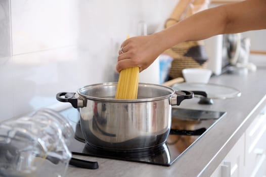 Close-up housewife's hand taking off wholegrain spaghetti from a container while cooking dinner in the home kitchen. Food background. Italian traditional meal