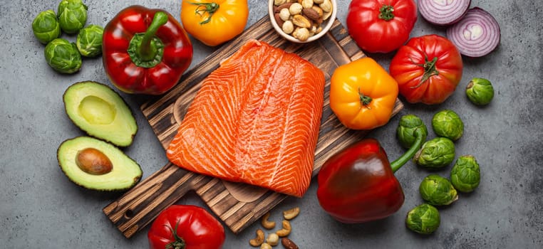 Fresh raw salmon fillet on wooden cutting board, organic bio vegetables and nuts on rustic stone grey background top view. Ingredients full of vitamins for healthy diet and nutrition