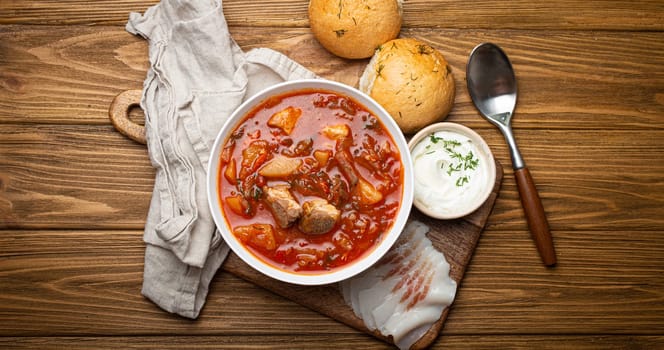 Ukrainian Borscht, red beetroot soup with meat, in white bowl with sour cream, garlic buns Pampushka and salo slices on rustic stone background. Traditional authentic dish of Ukraine