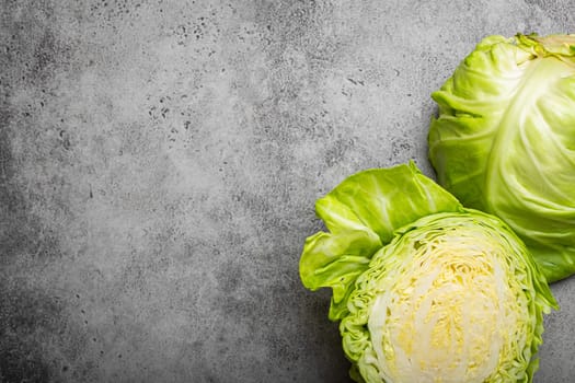 Fresh raw organic farm cabbage cut in half on grey rustic stone background top view, healthy cabbage in balanced nutrition and cooking concept. Space for text