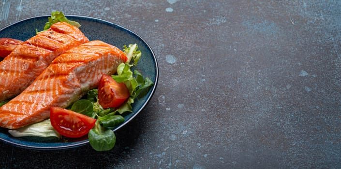 Grilled fish salmon steak with vegetables salad on ceramic plate on rustic stone background angle view, balanced diet or healthy nutrition salad meal with salmon and veggies, space for text