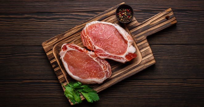 Cut raw meat pork steaks with seasonings on kitchen cutting board, rustic wooden background top view, ready for BBQ. Pork loin chops