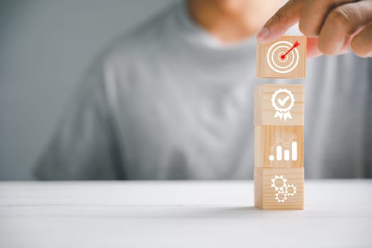 Businessman's hand with a wooden block cube and an icon, exemplifying company strategy development. Success and business goals concept.