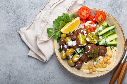 Falafel salad bowl with hummus, vegetables, olives, herbs and yogurt sauce. Vegan lunch plate top view on rustic stone background, healthy meal with falafel and veggies, space for text