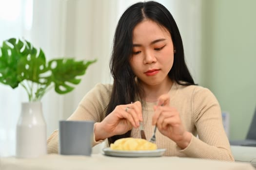 Shot of happy young woman eating homemade cream puff. People, food and lifestyle concept.