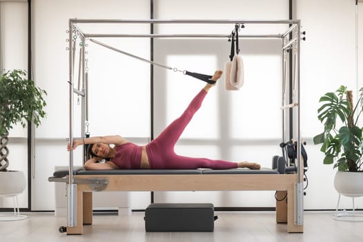 Asian woman doing pilates exercise on cadillac reformer machine