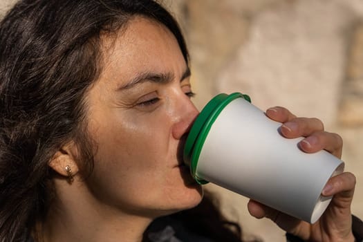 A middle-aged woman drinks coffee from a paper cup outside on a sunny autumn day. High quality 4k footage