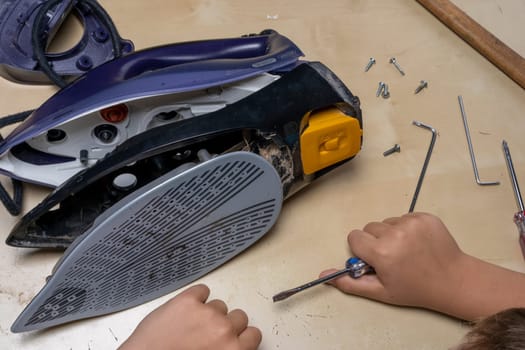 Disassembled electric iron. repairman checking and fixing broken iron. repairman checking and fixing broken steam ironusing simple tools. closeup