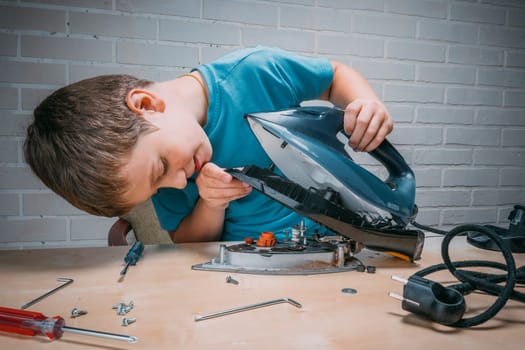 boy helps his mother. a funny master repairs an electric iron on the table using tools. Disassembled electric iron.