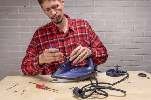 the ironing iron is broken. the master repairs the iron in the workshop on the table using tools. Disassembled electric iron.