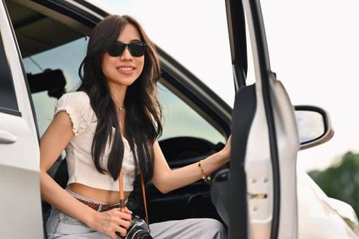 Attractive female tourist in sunglasses sitting in car with open door. Travel and vacation concept.