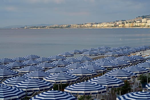 Striped blue and white umbrellas and sun loungers on the city beach. Umbrellas on the beach against the background of the sea