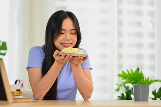 Shot of happy young woman eating homemade cream puff. People, food and lifestyle concept.