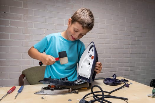 boy helps his mother. a funny master repairs an electric iron on the table using tools. Disassembled electric iron.